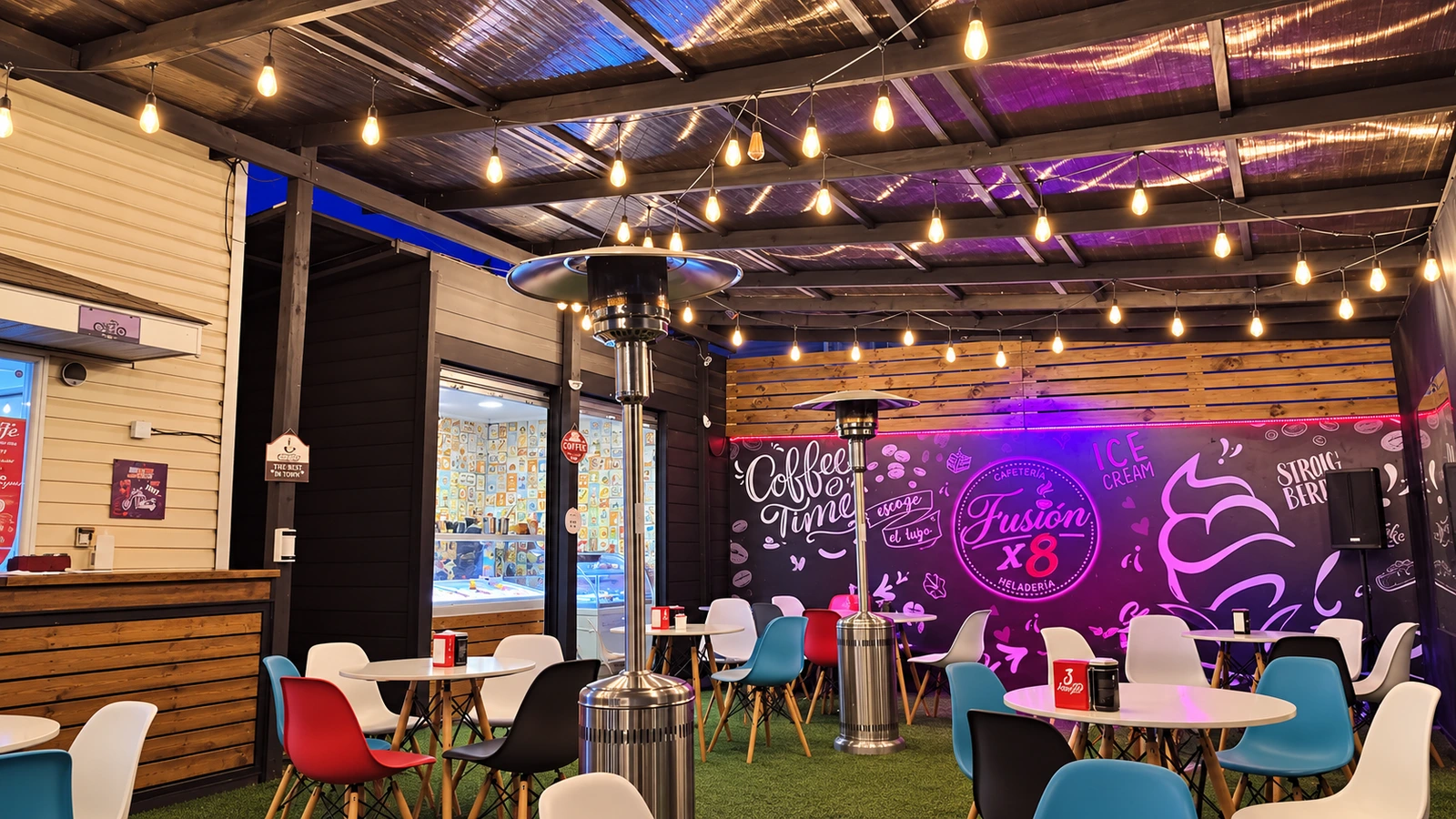 Salón de Fusión X8 con luces cálidas, mesas y el mural de la cafetería; fotografía editada para retirar personas y mejorar nitidez